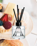 Belbora Candle Co Afternoon Tea Reed diffuser bottle with black sticks on a blurred dessert background