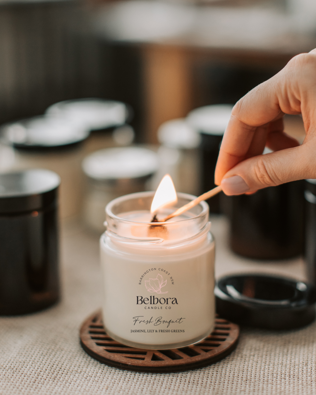 Person lighting a Belbora Candle Co Fresh Bouquet candle with a match on a textured surface.